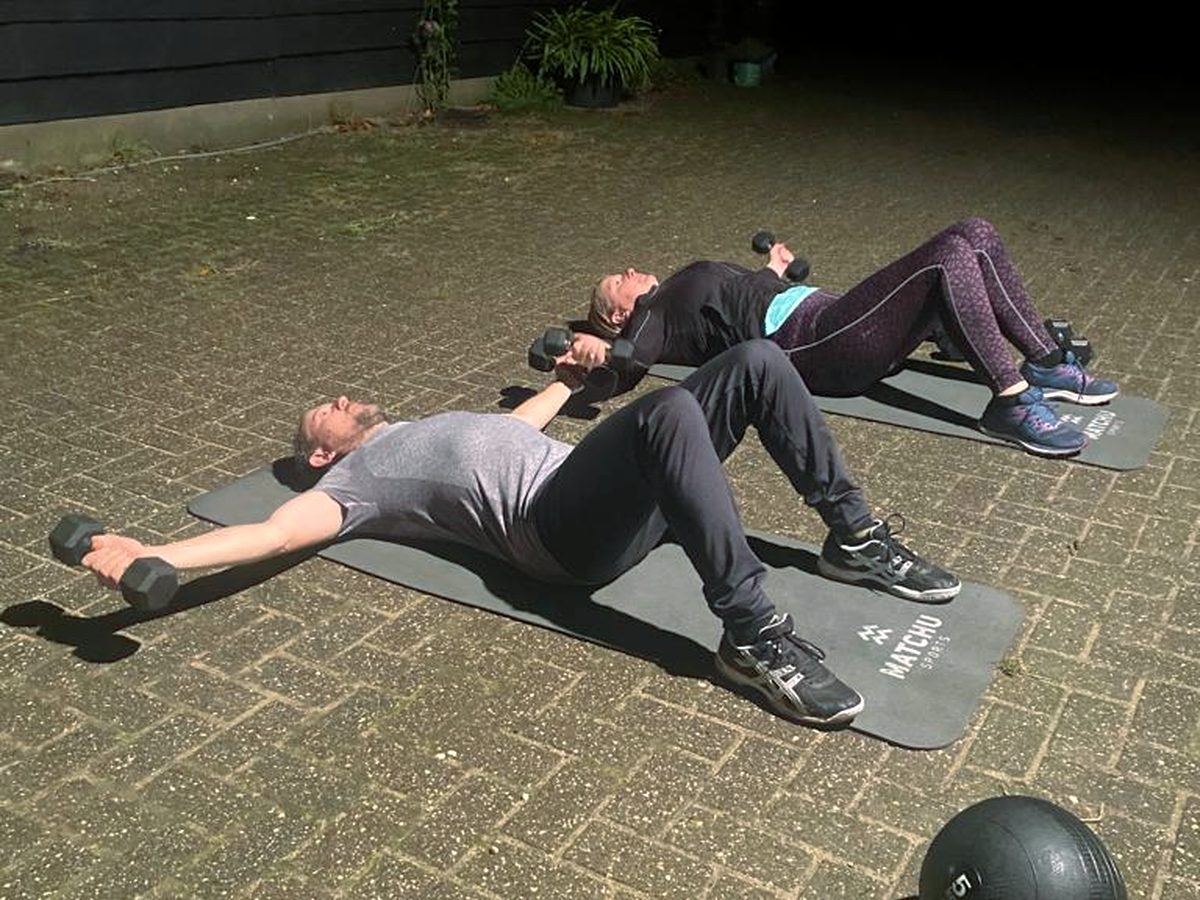 Drie mensen doen naast elkaar een liggende oefening met gewichten op matten