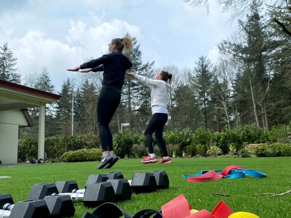 Twee mensen springen tegelijk omhoog tijdens een training op een grasveld met gewichten op de voorgrond