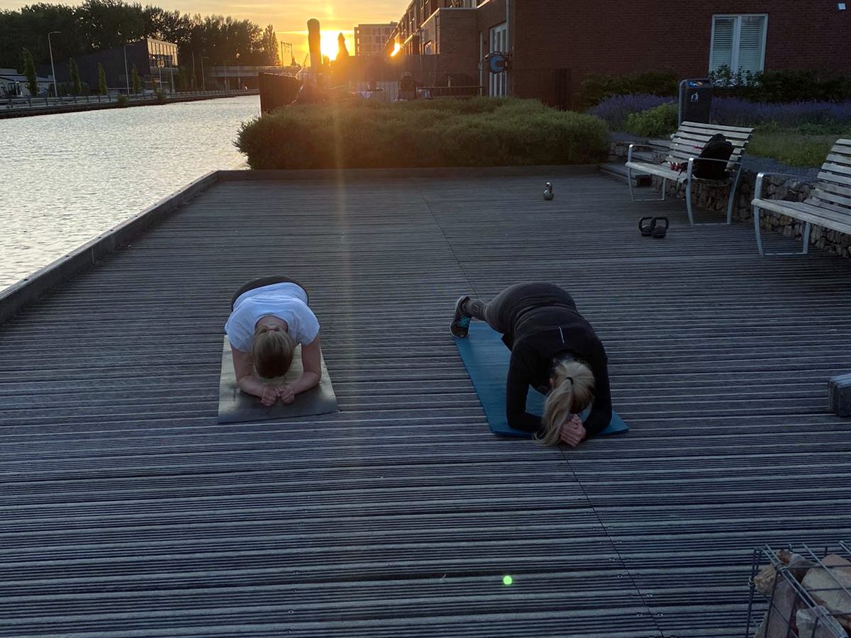 Twee mensen doen een oefening op een houten vlonder bij zonsopgang